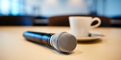 Persconferentie: microfoon en koffiekopje op een tafel.