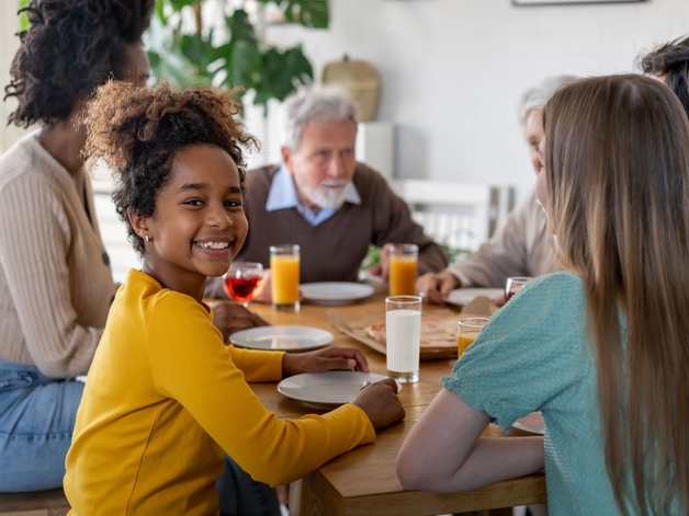 Jong meisje lachend naar de camera, terwijl ze zit te eten met haar familie.