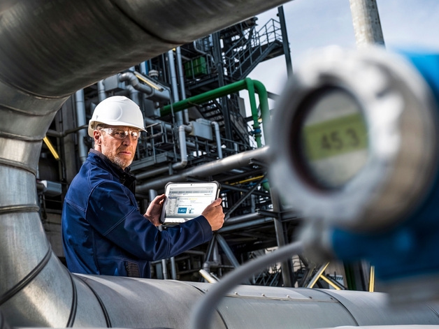 Technicus bezig met werkzaamheden op een industriële tablet in een raffinaderij.
